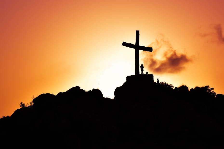 Majestic silhouette of a cross on a hill during a vivid sunset, symbolizing spirituality.